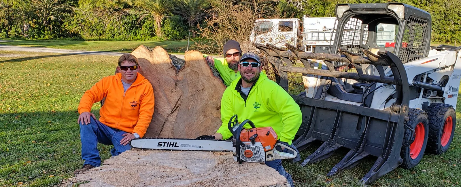 Three T&D crew members beside a large cut tree stump and clearing equipment