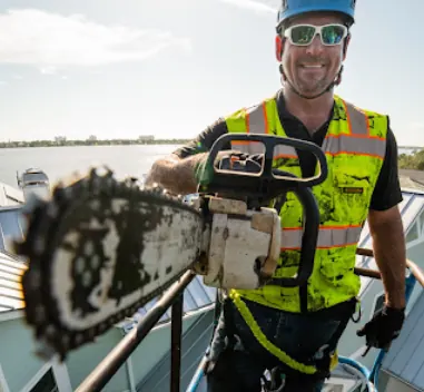 Tree service crew member wearing a helmet and high-visibility vest, holding a chainsaw